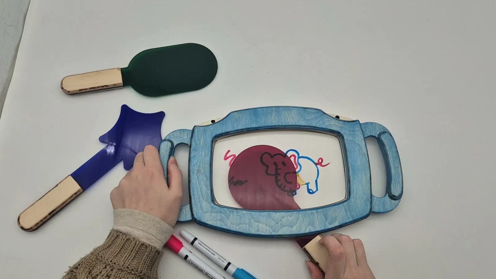Still from the product video: the magenta paddle slid over the drawing, hiding part of the elephant