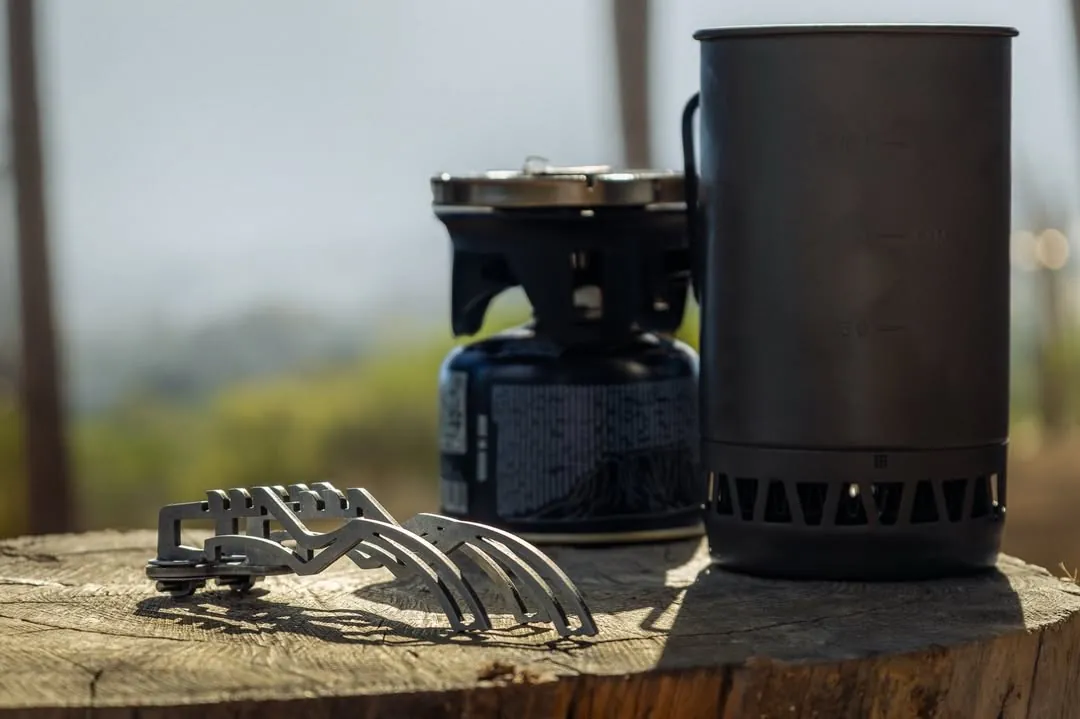 The stand beside a camping stove and titanium pot